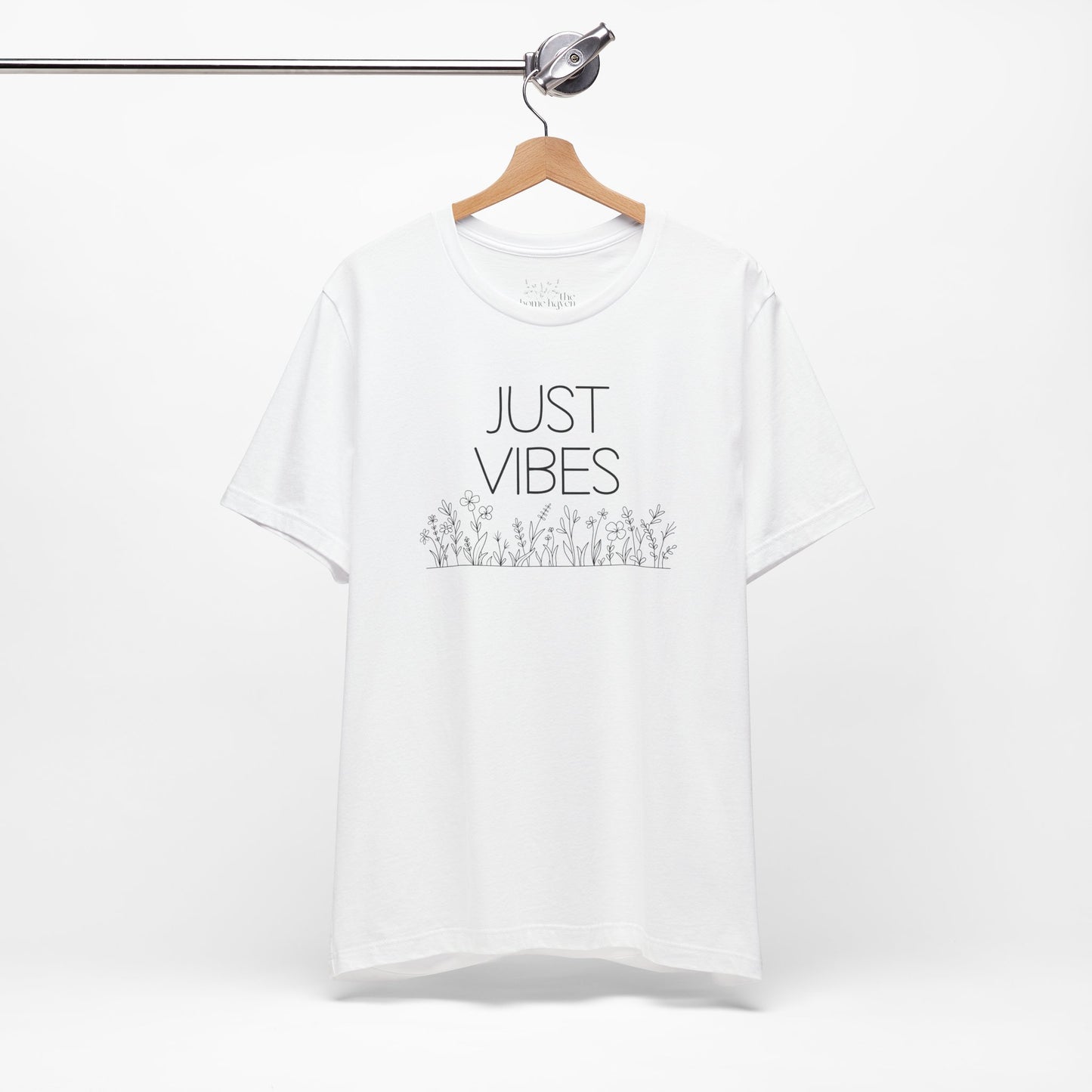 Just Vibes Graphic T-Shirt in white with minimalist floral design hanging on a wooden hanger against a white background.