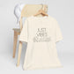 Just Vibes Graphic T-Shirt in cream color with minimalist floral design displayed on a wooden chair with a white cap.