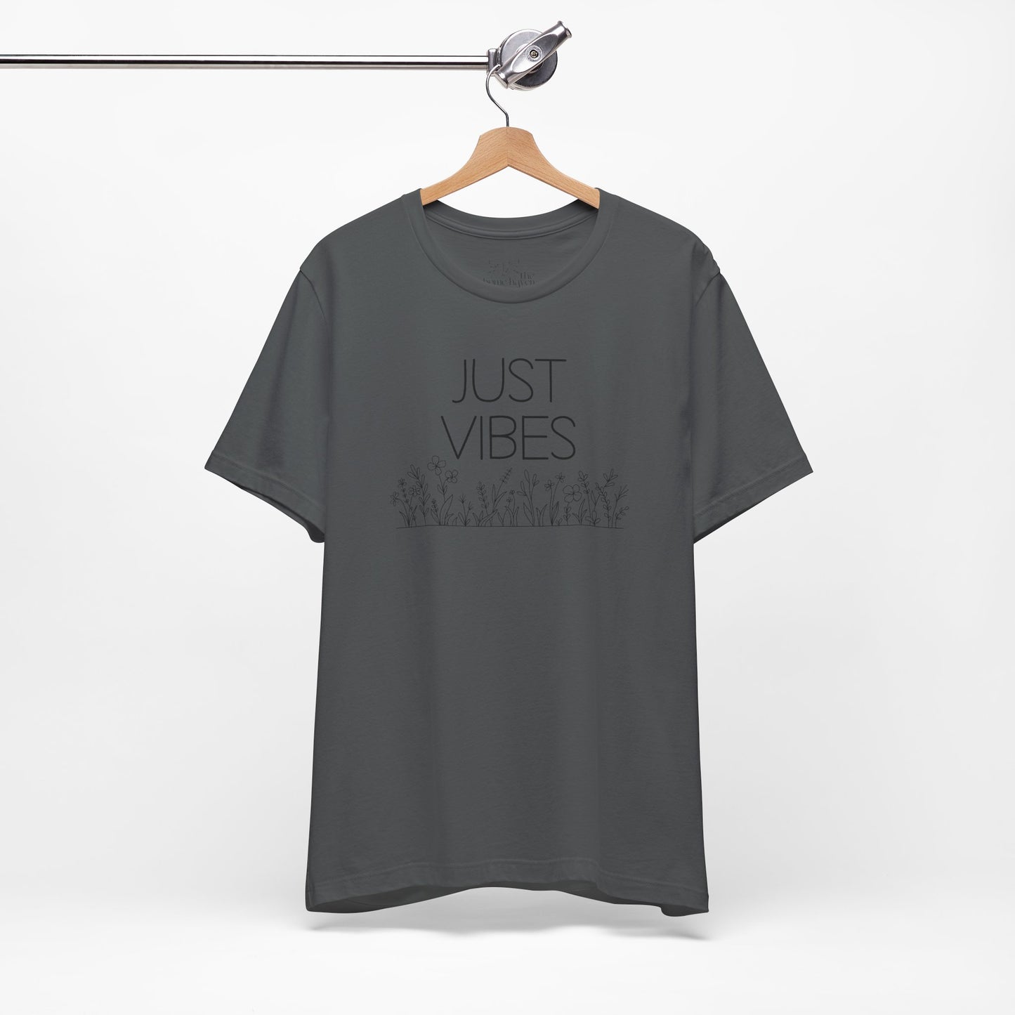 Just Vibes Graphic T-Shirt in dark gray with minimalist floral design hanging on a wooden hanger against a white background.