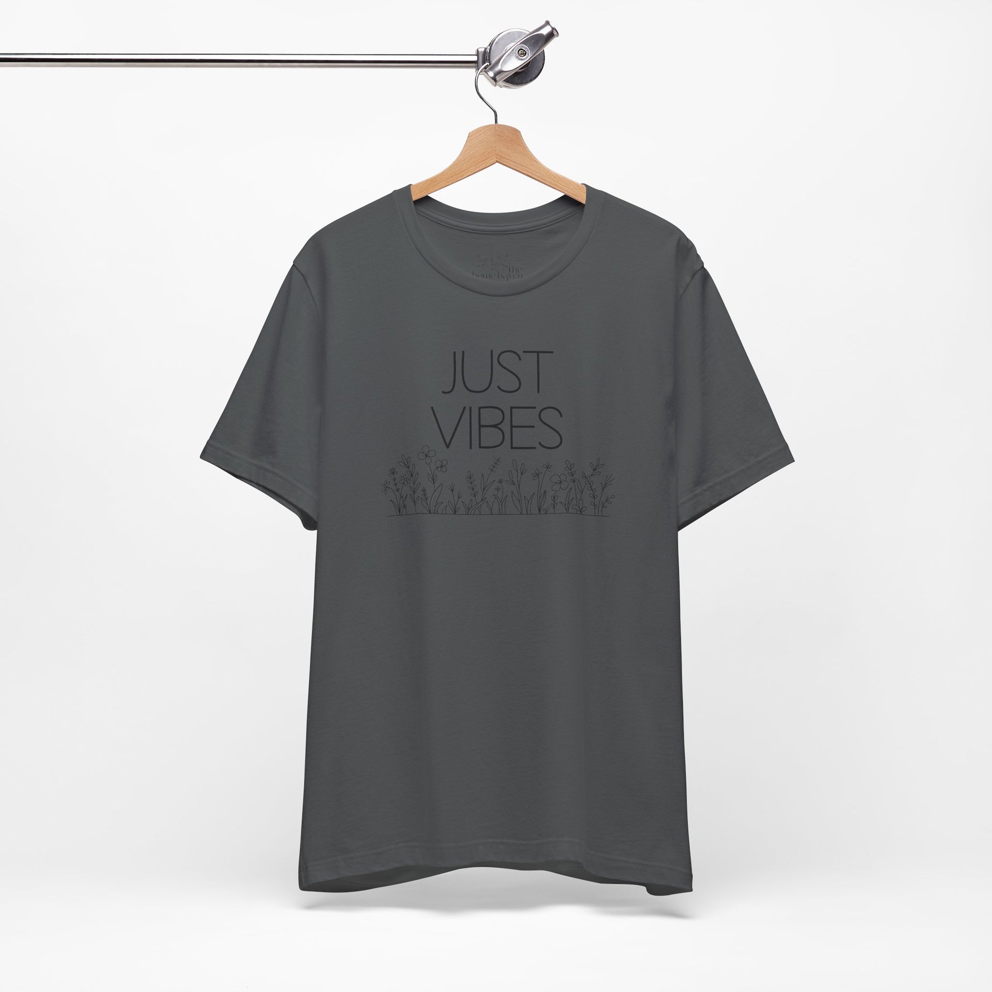 Just Vibes Graphic T-Shirt in dark gray with minimalist floral design hanging on a wooden hanger against a white background.