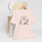 Light pink Wild and Free cactus graphic T-shirt draped over a chair, paired with a white cap for a relaxed and trendy look.