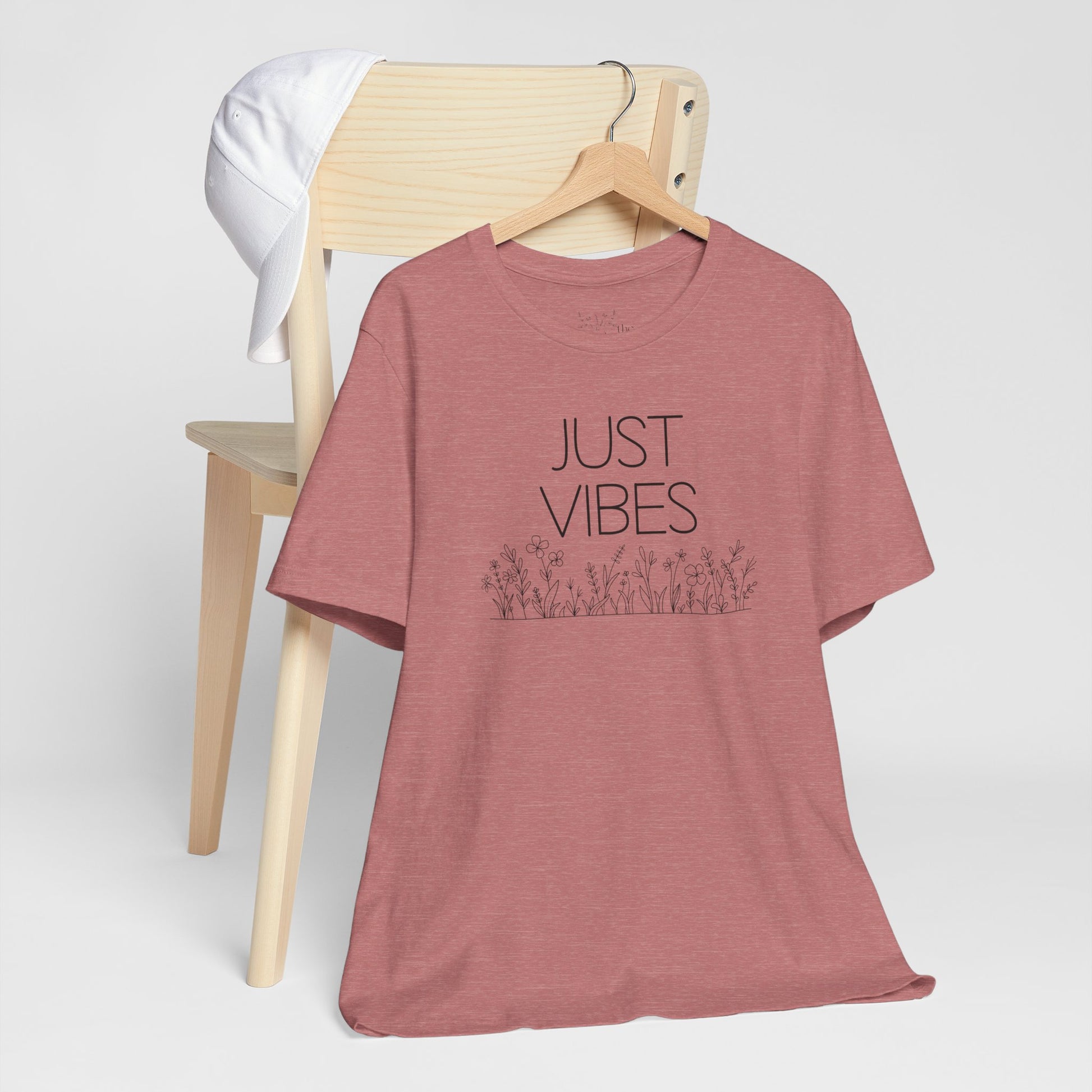 Just Vibes Graphic T-Shirt in dusty rose with minimalist floral design displayed on a wooden chair with a white cap.