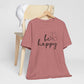 Be Happy graphic t-shirt in dusty rose with minimalist butterfly design displayed on a wooden chair with a white cap for a relaxed look.