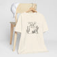 Cream Wild and Free cactus graphic T-shirt draped over a chair, styled with a white cap for a casual and nature-inspired outfit.