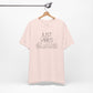 Just Vibes Graphic T-Shirt in light pink with minimalist floral design hanging on a wooden hanger against a white background.