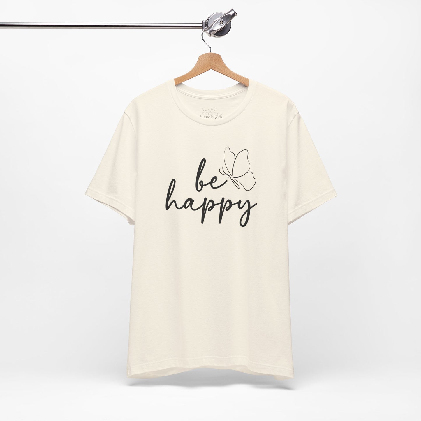 Cream Be Happy graphic t-shirt with minimalist butterfly design hanging on a wooden hanger, perfect for casual and chic outfits.