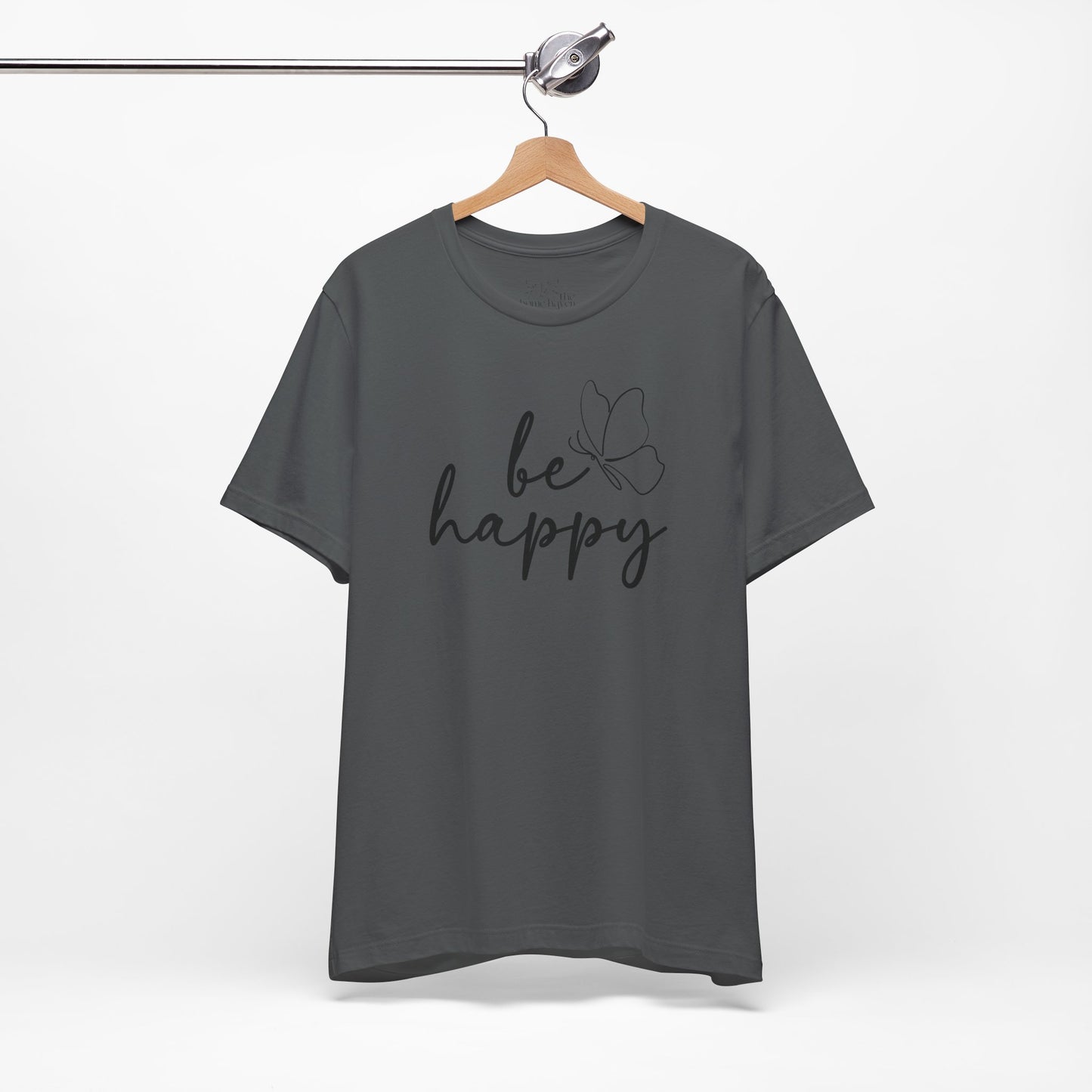 Charcoal gray Be Happy graphic t-shirt with minimalist butterfly design hanging on a wooden hanger for a sleek and modern style.