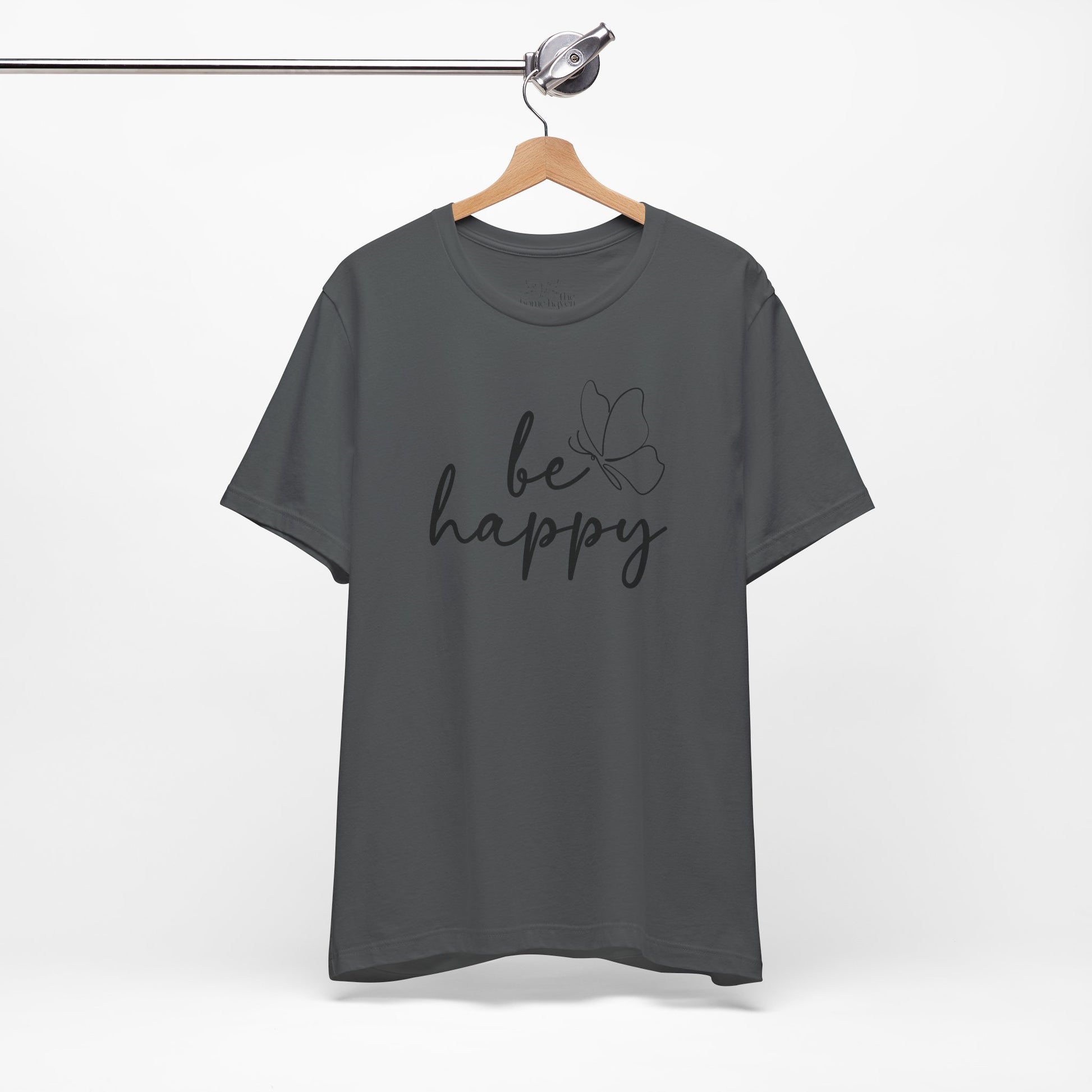 Charcoal gray Be Happy graphic t-shirt with minimalist butterfly design hanging on a wooden hanger for a sleek and modern style.
