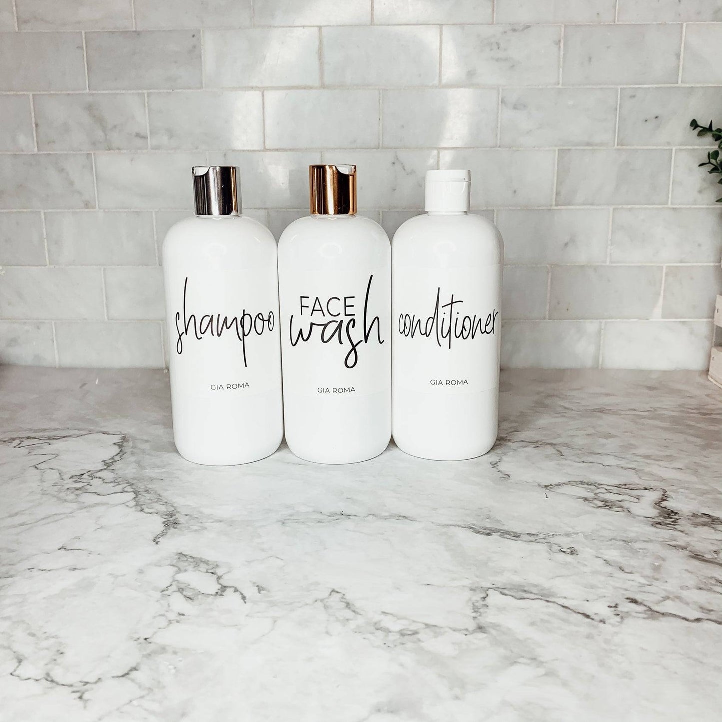 Three 16oz white PET bottles labeled shampoo, face wash, and conditioner with silver and gold flip tops. Minimalist bathroom dispensers.