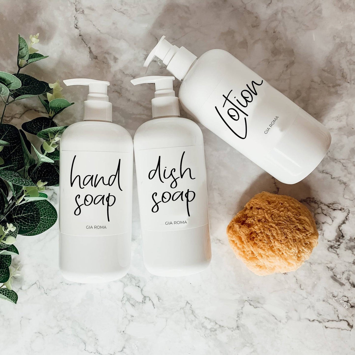 Three 16oz white PET pump bottles labeled hand soap, dish soap, and lotion. Reusable dispensers with a sponge on a marble countertop.