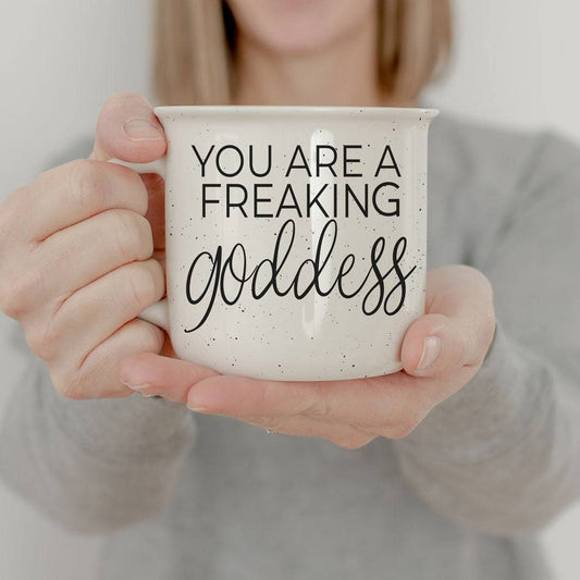 14.5oz ceramic coffee mug with 'You Are a Freaking Goddess' design, held by a woman in a casual gray outfit.