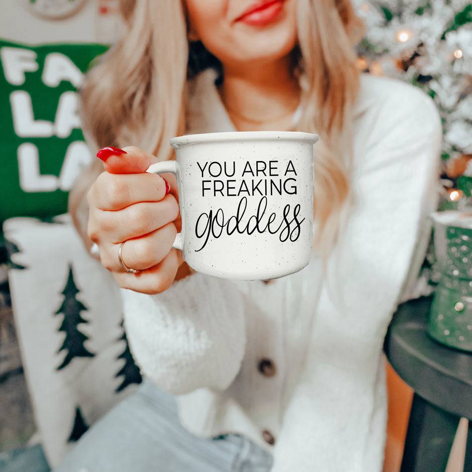 14.5oz ceramic coffee mug with 'You Are a Freaking Goddess' inspirational quote, held by a woman in a cozy holiday setting.