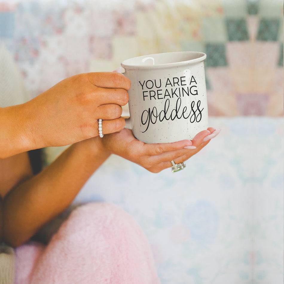 14.5oz ceramic coffee mug with 'You Are a Freaking Goddess' quote, held by a woman with elegant jewelry in a cozy setting.