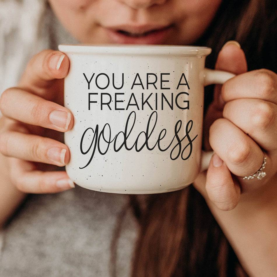 14.5oz ceramic coffee mug with 'You Are a Freaking Goddess' inspirational design, held close by a woman enjoying her drink.