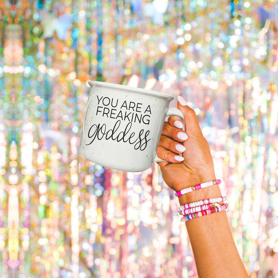 14.5oz ceramic coffee mug with 'You Are a Freaking Goddess' design, held by a hand against a sparkling, festive background.