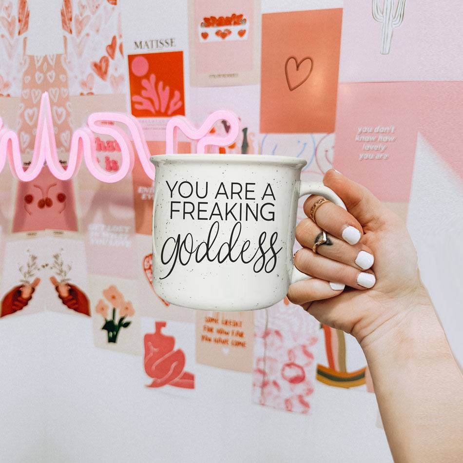 14.5oz ceramic coffee mug with 'You Are a Freaking Goddess' quote, held in front of a pink and red Valentine's Day-themed wall.