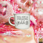 14.5oz ceramic coffee mug with 'You Are a Freaking Goddess' quote, placed on a table with pink festive decor.